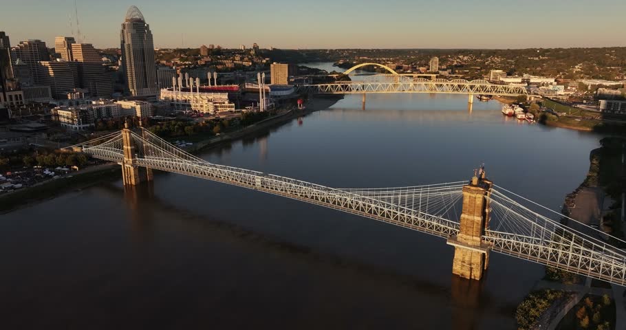Aerial view of the John A. Roebling Suspension Bridge spanning the Ohio River with the Cincinnati skyline in the background at sunset in Cincinnati, Ohio, United States.
