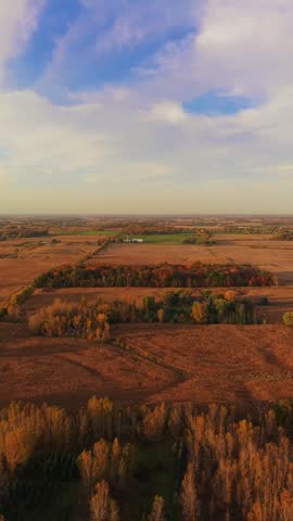 A vertical aerial shot showcasing the vibrant fall colors of Wisconsin farmland and forests under a warm sunset sky. Perfect for social media marketing and travel content.