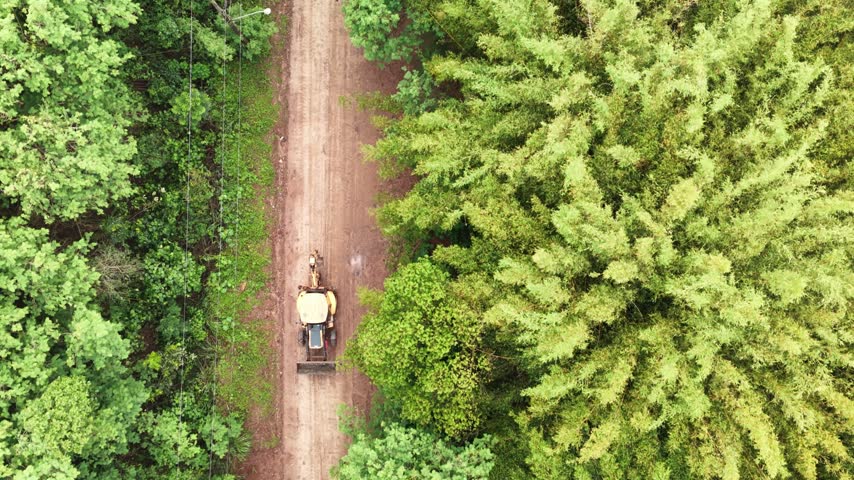 Aerial view of a tractor driving on a dirt road through a lush forest in Araras, Sao Paulo, Brasil.