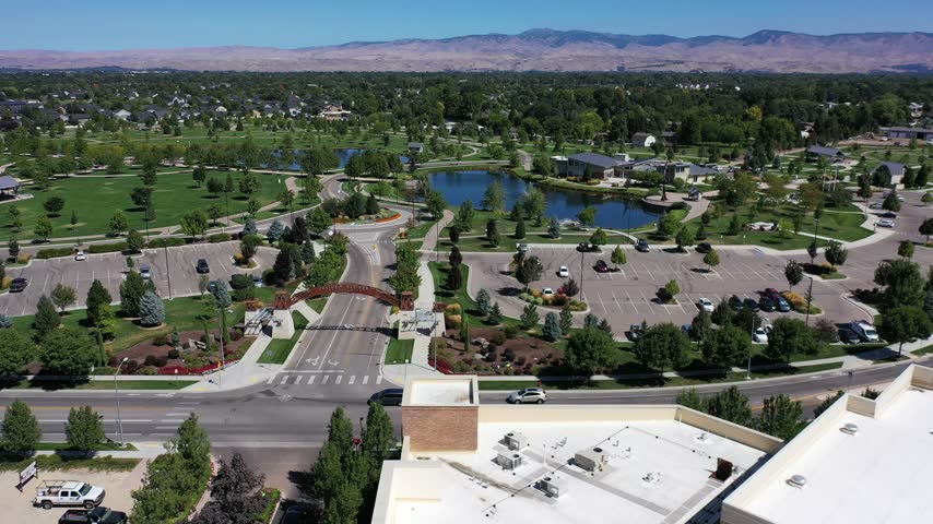 Aerial drone view of a landscaped park with ponds, curving paths and green lawns in Meridian, Idaho, with mountains beyond.