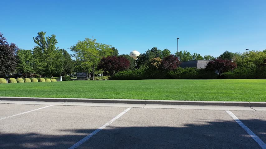 Low drone shot skimming a green lawn toward a line of trees on a clear sunny morning in a Meridian, Idaho park.