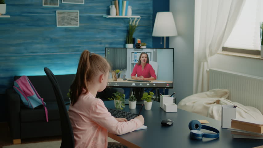 Notes, teacher and schoolgirl during a remote video lesson at home, with the child writing in a notebook while following the screen for online class, digital education and focused learning