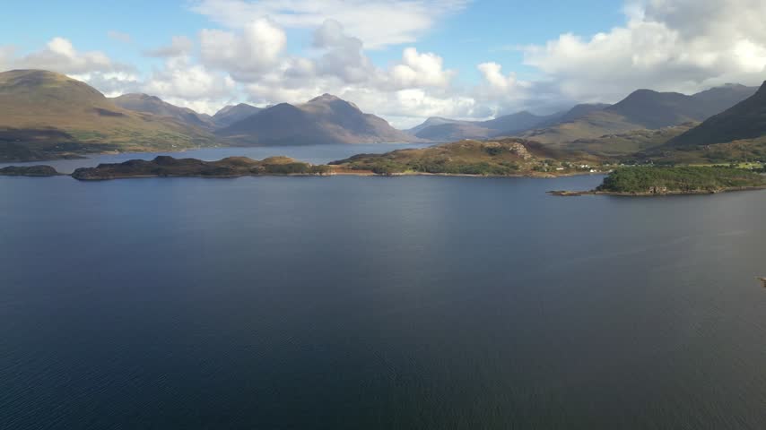 Aerial view of tranquil bay and rugged hills under scattered clouds in rural Scotland