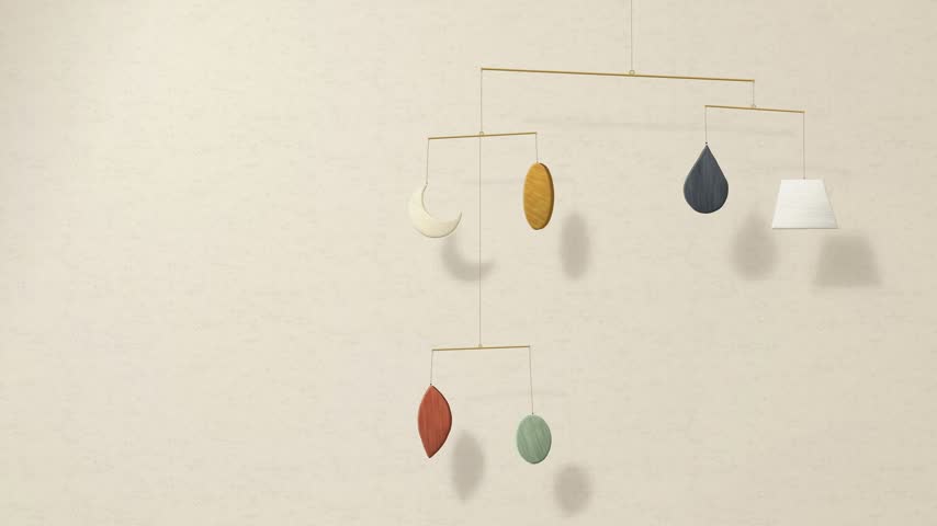 Mid century kinetic mobile of painted wood shapes on thin brass rods turning slowly before a warm cream plaster wall with soft window shadows