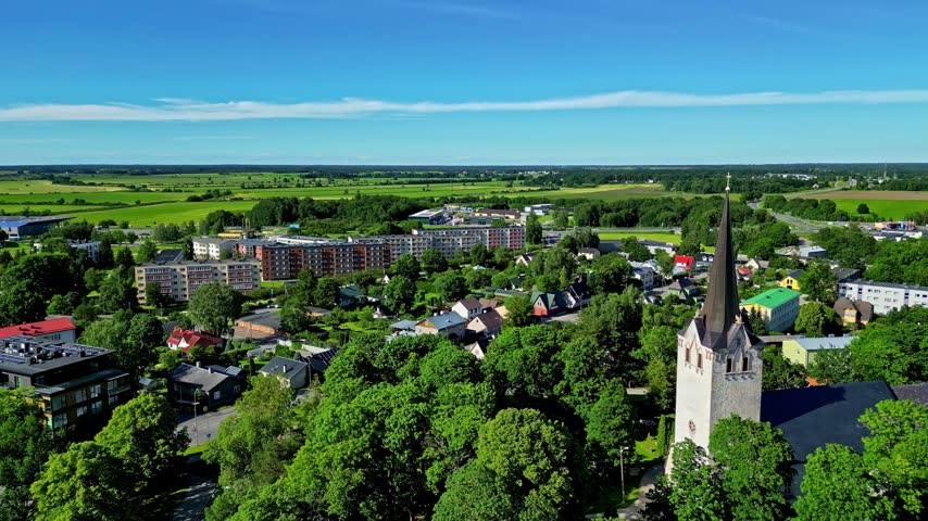 Aerial view of a historic church with a tall spire surrounded by lush trees and residential buildings in a small town in Estonia.