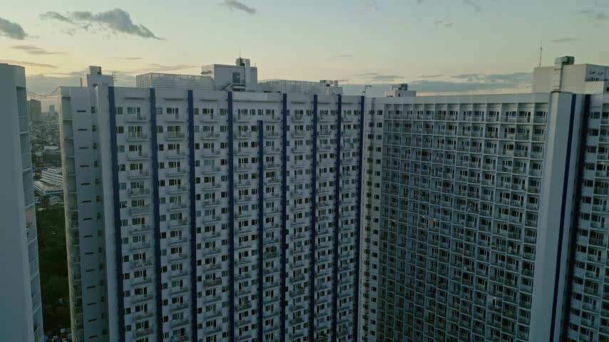 Aerial view of modern high-rise residential apartment buildings with balconies and glass windows under a soft evening sky in Manila, Metro Manila, Philippines.