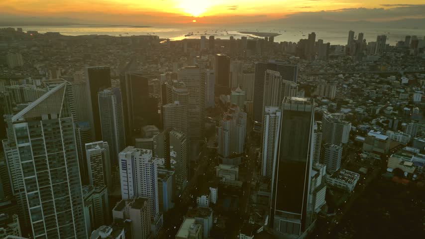 Aerial view of the Manila skyline at sunset, featuring modern skyscrapers, dense urban buildings, and the golden light reflecting over the bay in Manila, Metro Manila, Philippines.