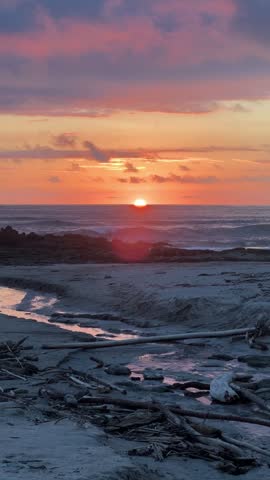 Vertical static view over driftwood beach with tidal stream and waves to sunset over the Pacific Ocean, Nicoya Peninsula, Costa Rica