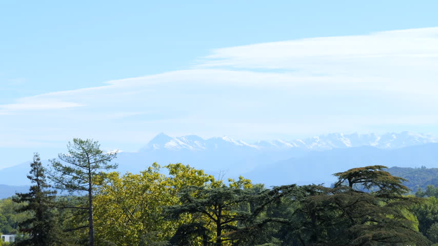 Subtle zoom in on distant Pyrenees mountains and trees viewed from Pau, France, with negative space sky. Concept of nature, travel, and mountain landscape.