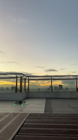 Vertical static view of a drone taking off from a rooftop deck as a man walks to the railing in silhouette above the city at dawn, Manila, Philippines