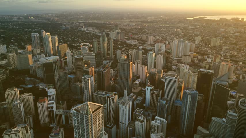 Aerial view of Manila skyscrapers bathed in golden hour light with dense urban architecture and high-rise buildings in Manila, Metro Manila, Philippines.