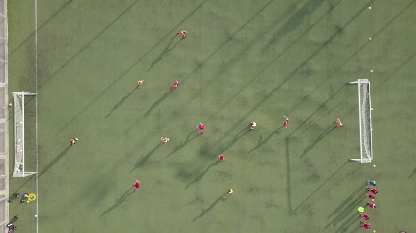 Aerial view of a soccer match with players in red and yellow jerseys on a green field in Israel.