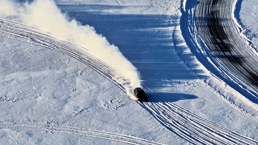 Aerial view of a car drifting on a snow-covered track, creating tire marks on the frozen surface in Latvia.