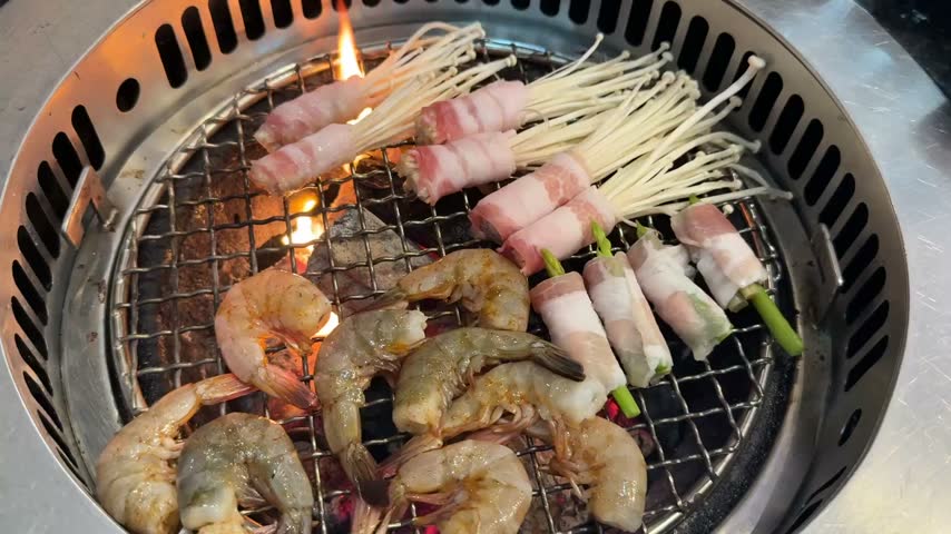 Fresh prawns, bacon-wrapped enoki mushrooms, and bacon-wrapped asparagus grilling over hot charcoal