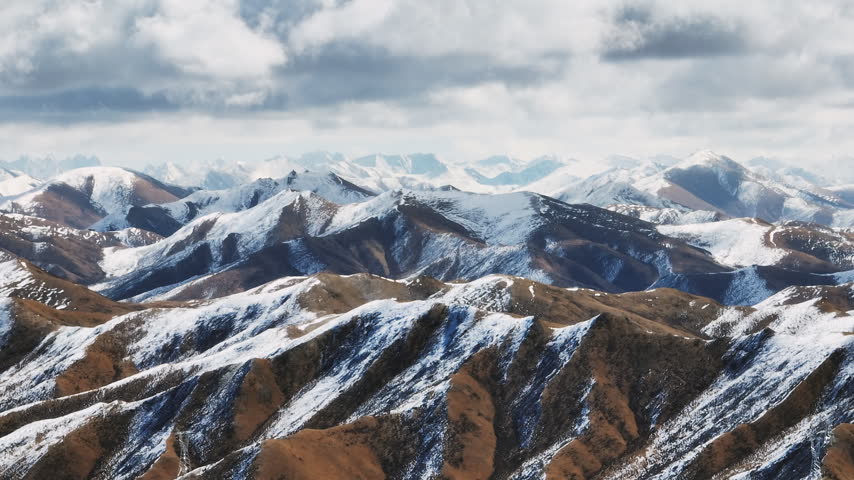 Rolling snow covered ridges under heavy cloud, brown slopes alternating with white snow fields