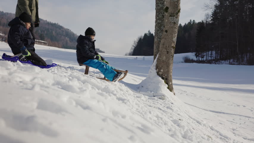 Two children sledding down a snowy hill with their father, enjoying an exciting outdoor family activity together on a winter day.