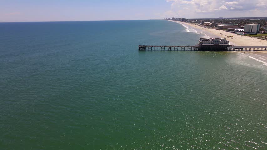 An aerial flight approaches the pier above coastal water in Daytona Beach.