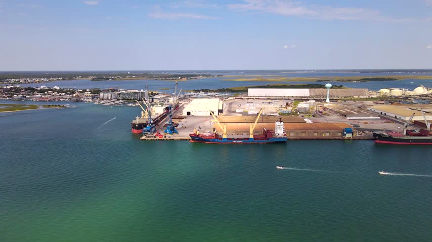 Motorboats leave white wakes across the water beside docked Morehead City cargo ships.