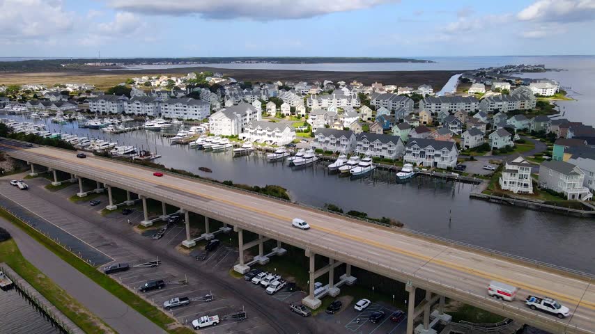 Cars cross an elevated bridge beside moored yachts and waterfront housing near Manteo.