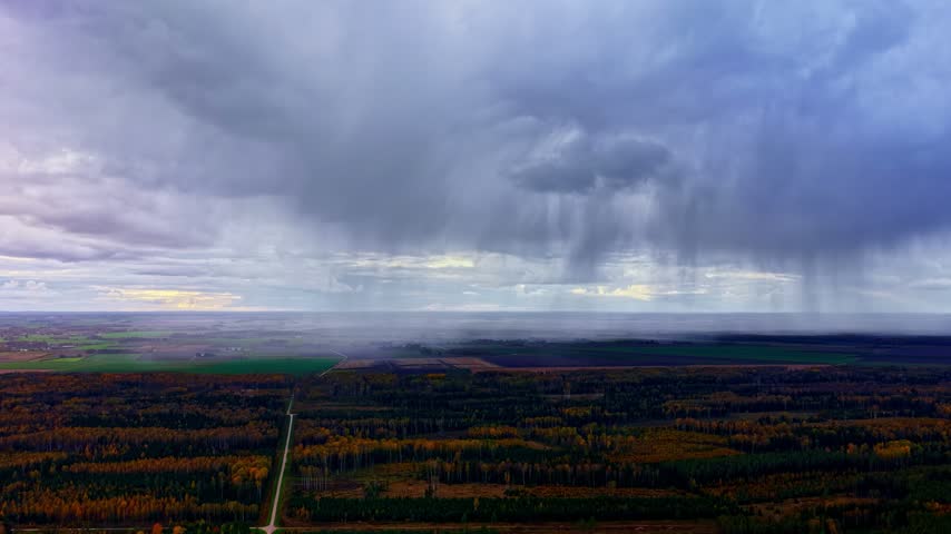 Aerial view of heavy rain clouds gathering over the vast forest landscape with a straight road cutting through the trees in Latvia.