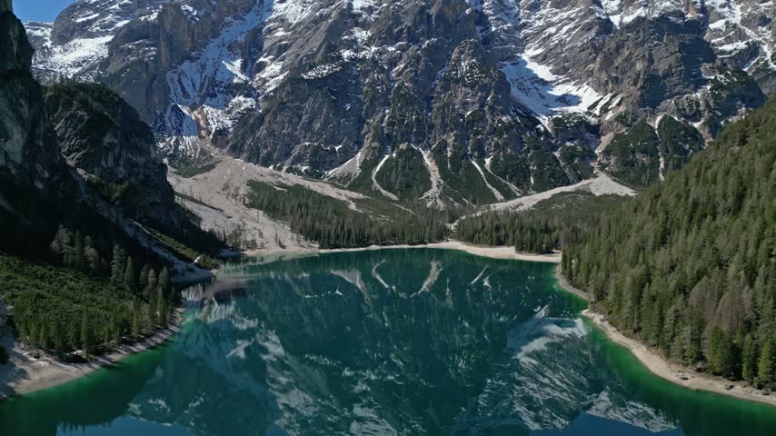 Aerial view of Pragser Wildsee surrounded by towering snow-capped mountains and dense pine forests in Prags, Trentino-Alto Adige, Italy.