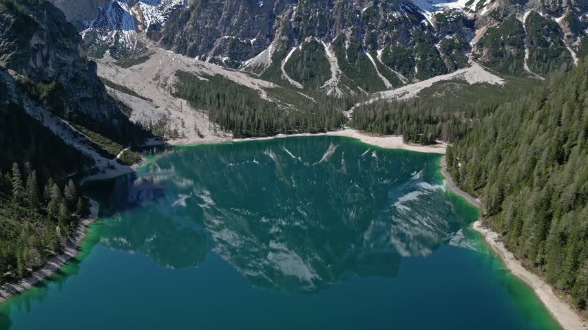 Aerial view of the turquoise waters of Pragser Wildsee surrounded by dense pine forests and steep mountain peaks in Prags, Trentino-Alto Adige, Italy.