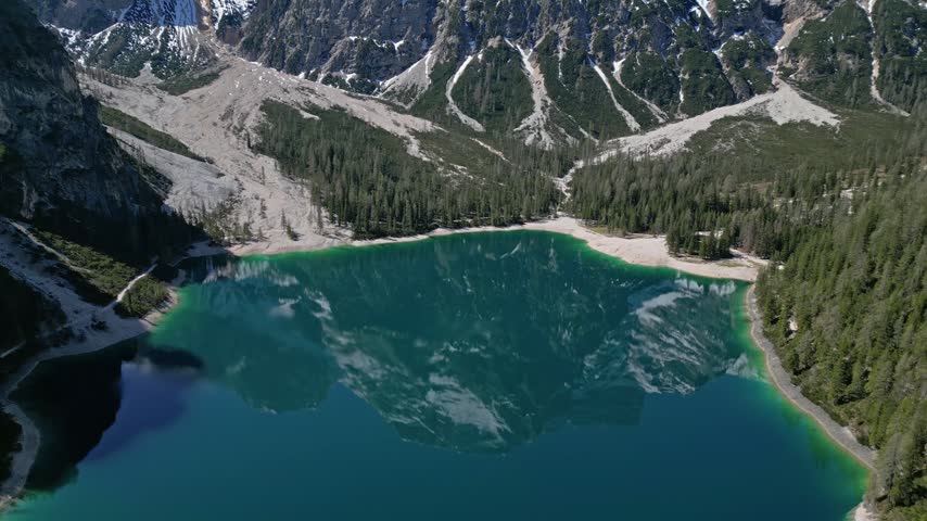 Aerial view of the turquoise waters of Pragser Wildsee surrounded by dense pine forests and steep mountain peaks in Prags, Trentino-Alto Adige, Italy.