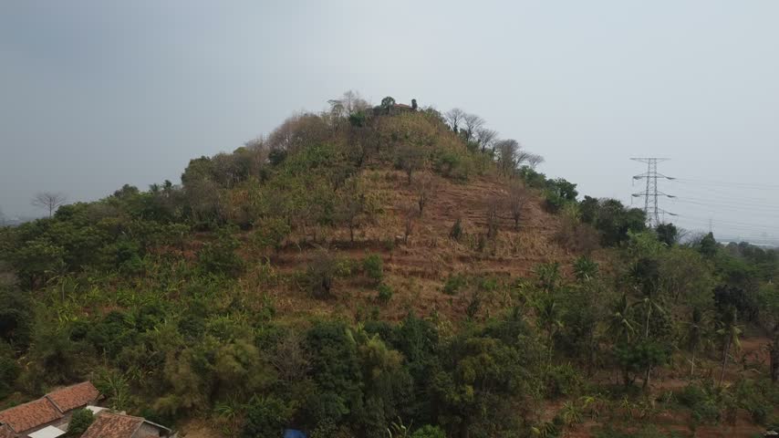Aerial view of a dry, terraced hill with sparse vegetation located right behind a dense residential area.