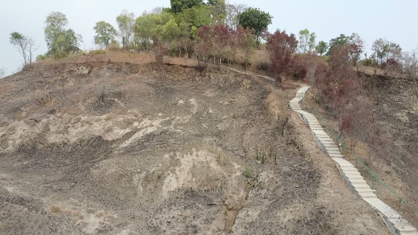 Aerial view slowly ascending along a newly constructed concrete staircase built on a dry, barren hillside.