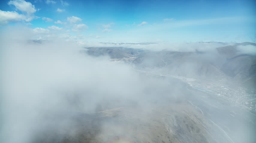 A river of low cloud pouring over a mountain ridge while a small plateau town appears through the gaps below