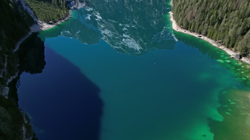 Aerial view of the turquoise waters of Pragser Wildsee surrounded by dense pine forests and steep mountain cliffs in Prags, Trentino-Alto Adige, Italy.