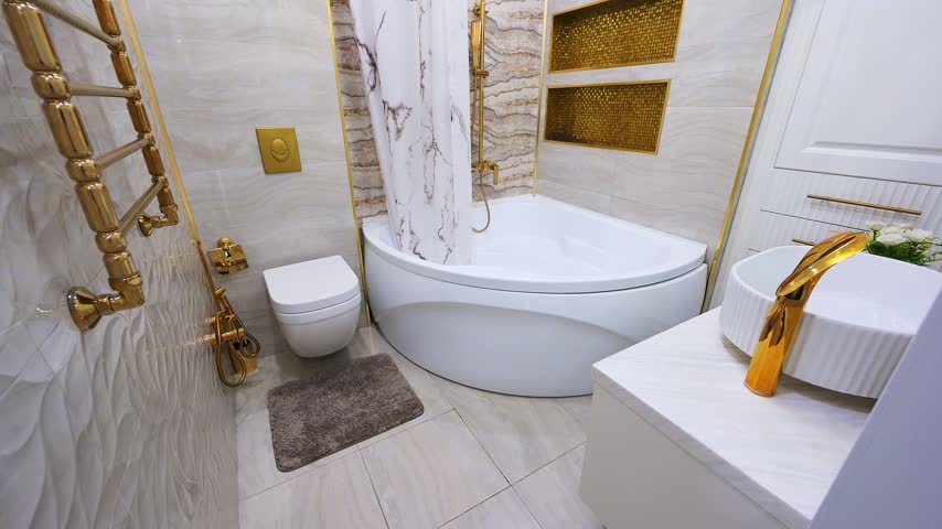 Stylish bathroom with white curved bathtub, gold fixtures, marble tiles, recessed niches, and ornate towel radiator.
