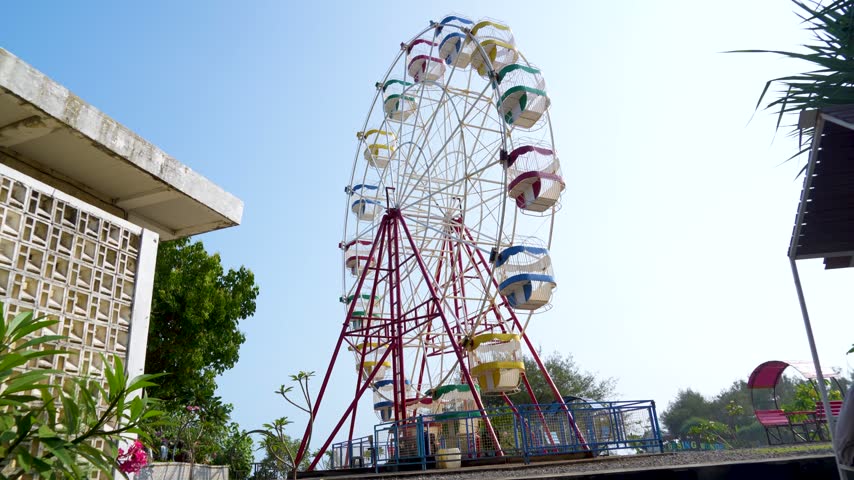 A classic colorful ferris wheel against a bright blue sky surrounded by green trees in a park.