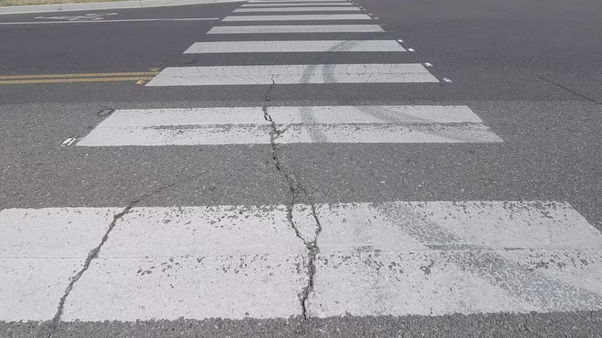 Faded and cracked white crosswalk paint marks a pedestrian street intersection