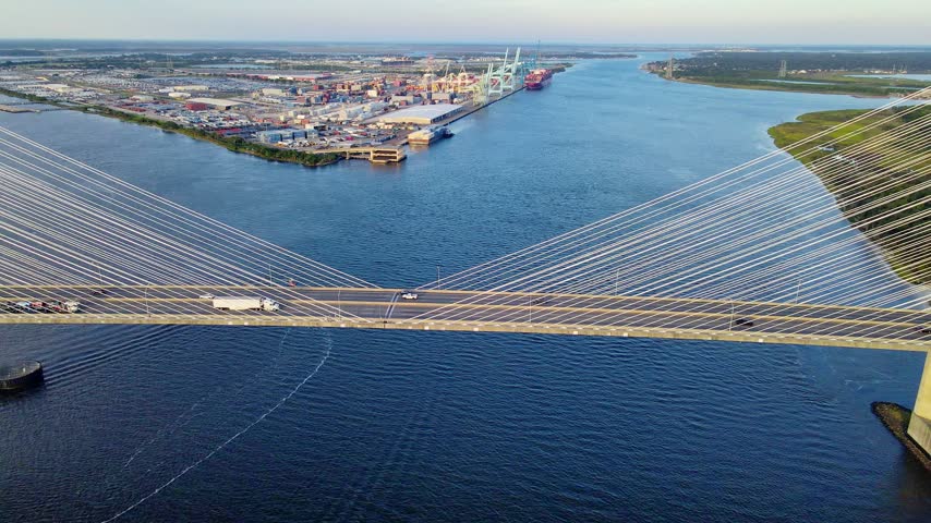 cable bridge extends across the Jacksonville river beside port infrastructure and forest.