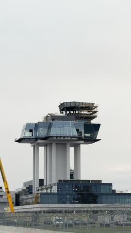 Modern airport control tower under construction with glass facade and scaffolding under overcast sky and security fence