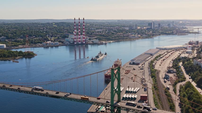 Witness the impressive sight of a military ship being towed gracefully through Halifax Harbour in Nova Scotia, Canada. The picturesque landscape showcases the vibrant city and serene waters.