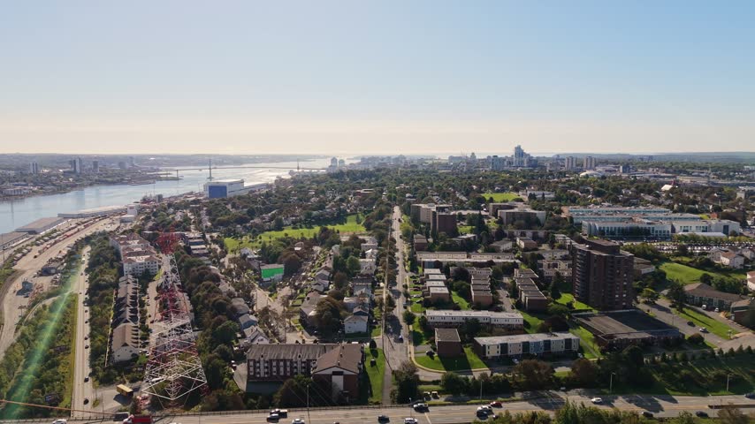 Experience the stunning aerial perspective of Halifax, Nova Scotia, showcasing the unique architecture, lush greenery, and vibrant waterfront. The city unfolds beautifully under the bright sun.