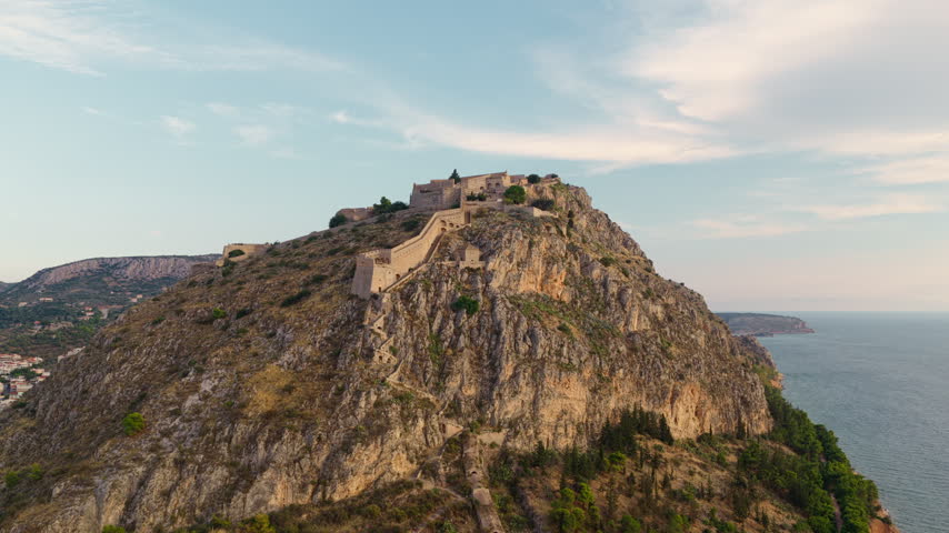 Aerial view of the venetian Palamidi fortress on a rocky hill in Nafplio, Greece during golden hour, revealing the city and Argolic Gulf in the Peloponnese region