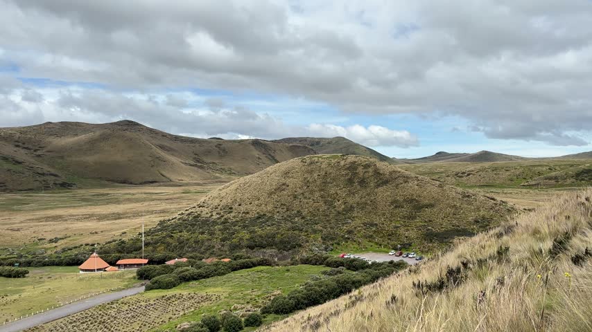 Panning view starting from a dirt hiking trail through paramo grass across the valley towards a mountain lake