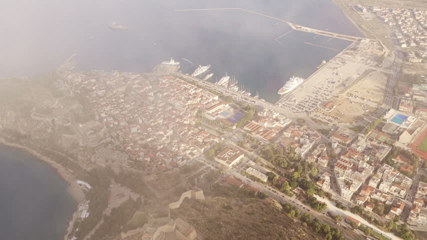Stunning aerial perspective revealing the beautiful historic city of Nafplio in Greece, showing the old town, Palamidi fortress, and harbor with docked yachts as the view clears from the clouds