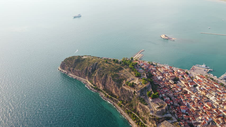 Stunning aerial perspective of the historic old town of Nafplio in Greece, showing the Akronauplia fortress on a rocky peninsula surrounded by the calm, turquoise waters of the Aegean Sea