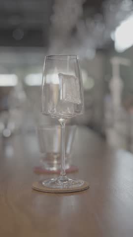 Bartender pouring a freshly mixed cocktail into a stemmed glass filled with ice on a wooden bar counter, capturing professional mixology and beverage preparation.