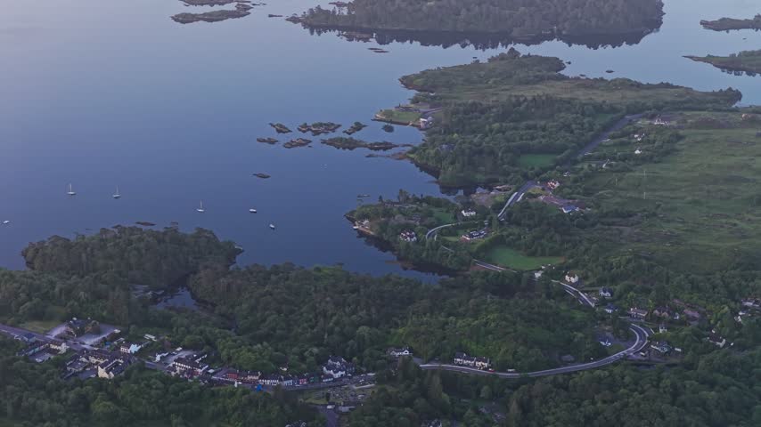 A broad aerial view crosses the sheltered waters and wooded islands of Glengarriff Harbour in West Cork, Ireland. Small boats and scattered coastal homes frame the calm inlet at the head of Bantry Bay on the Beara Peninsula.