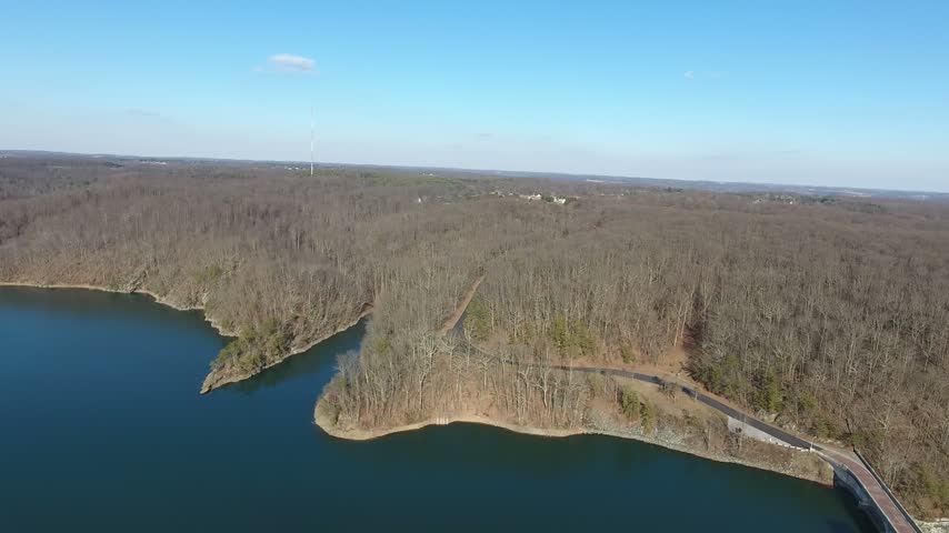 Aerial slow pan along the bare wooded shoreline and peninsulas of Prettyboy Reservoir on a clear winter day, with blue water and leafless forest under a blue sky. Baltimore County, Maryland, USA.