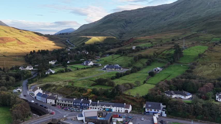 Aerial view of Leenaun village with traditional houses, a stone bridge and winding roads beneath rugged mountains in Connemara.