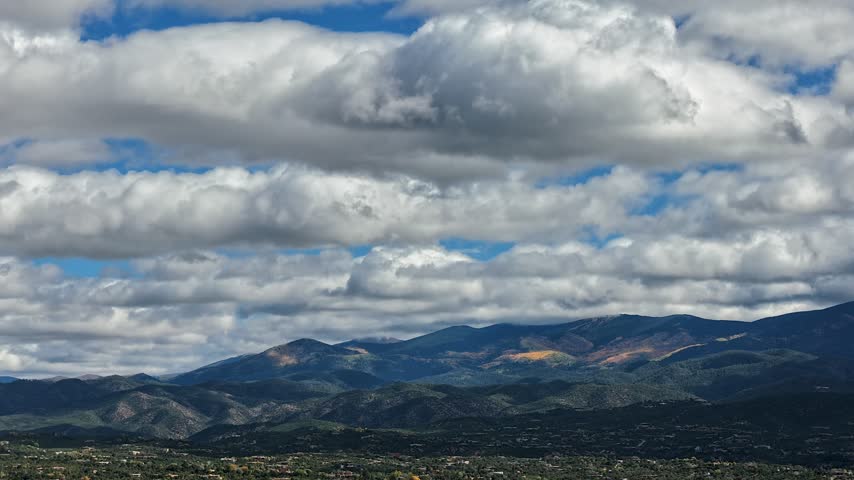 Aerial view of fast moving clouds above the Santa Fe foothills with mountains speckled gold with fall colors in Santa Fe, New Mexico, United States.