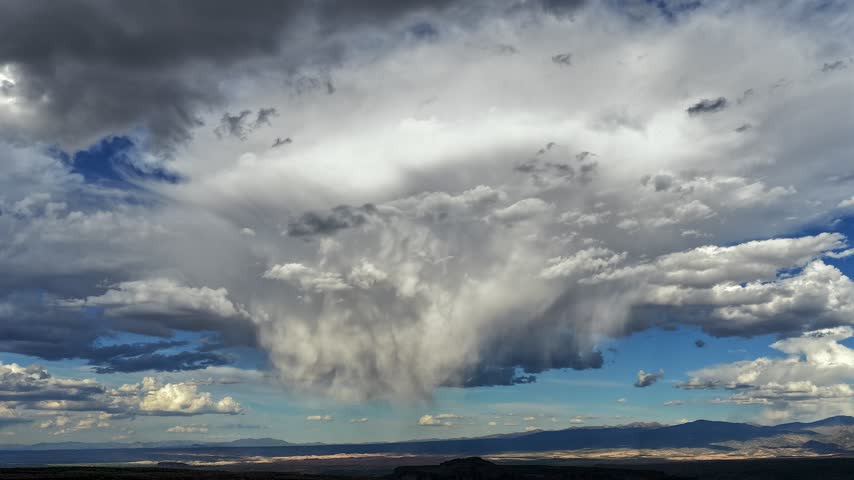 Aerial view of a large rain cloud formation resembling an underwater creature drifting over a dark canyon landscape in White Rock, New Mexico, United States.