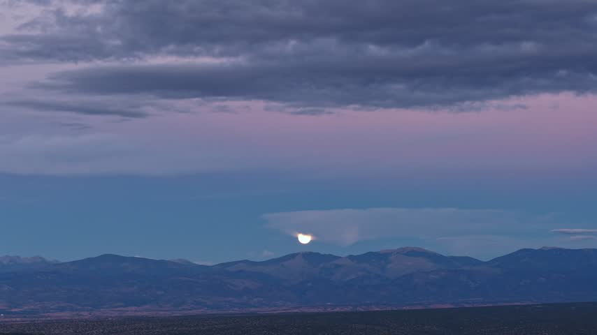Aerial view of the moon rising through a cloud layer with purple evening colors above Mount Baldy in Santa Fe, New Mexico, United States.