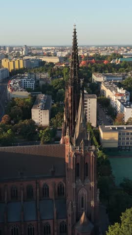 Gothic church tower with spire rises above colorful cityscape of Wroclaw, Poland, showcasing historical architecture and urban landscape in golden hour light
